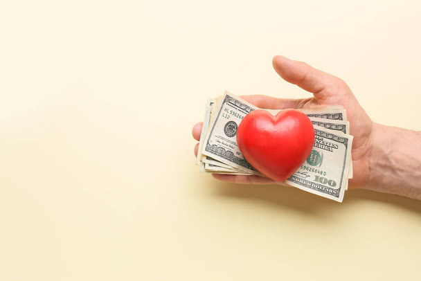Mano masculina con dinero y corazón rojo sobre fondo de color. Concepto de donación - Foto, imagen