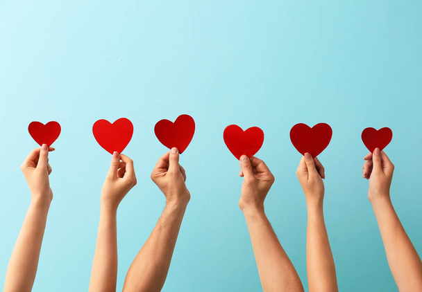 Mannelijke en vrouwelijke handen met rode papieren harten op kleur achtergrond. Donatieconcept - Foto, afbeelding