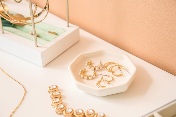 Tray with different earrings on white table near color wall - Photo, image