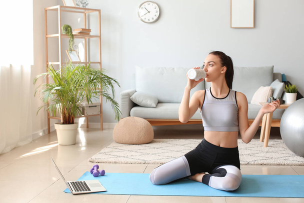 Young woman in sportswear drinking water after training at home - Photo, Image