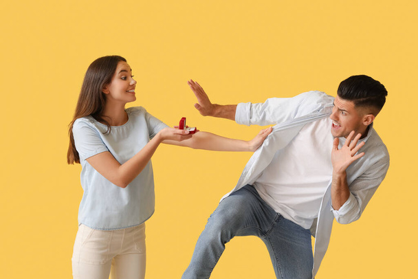 Giovane donna sollecitando il suo fidanzato spaventato a impegnarsi su sfondo di colore - Foto, immagini