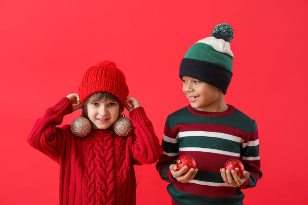 Niedliche kleine Kinder in Winterpullovern und mit Weihnachtskugeln auf farbigem Hintergrund - Foto, Bild