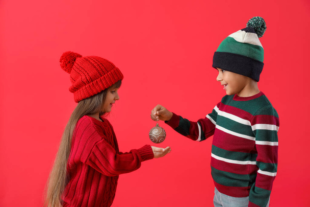 Cute little children in winter sweaters and with Christmas ball on color background - Фото, изображение