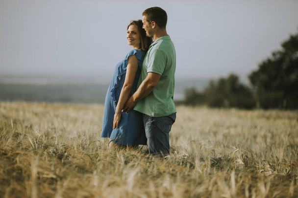Young husband and his pregnant wife in the sunny summer field - Foto, imagen