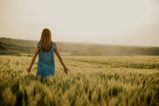 Вид сзади на молодую беременную женщину в синем платье в летнем поле - Фото, изображение