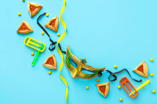 Máscara de carnaval y galletas Hamantaschen con sonajeros para vacaciones Purim sobre fondo de color - Foto, imagen