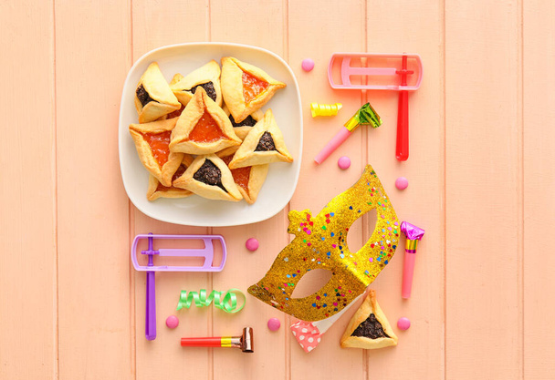 Máscara de carnaval y galletas Hamantaschen con sonajeros para vacaciones Purim sobre fondo de madera de color - Foto, imagen