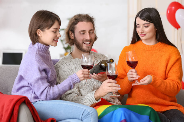 Άντρας και δύο όμορφες γυναίκες πίνουν κρασί στο σπίτι. Έννοια της πολυαμορίας - Φωτογραφία, εικόνα