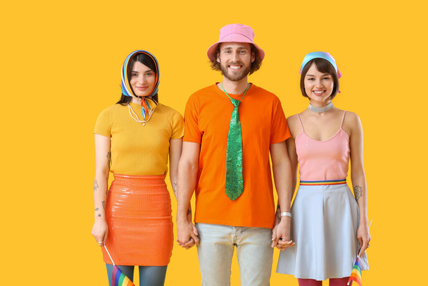 Man and two beautiful women in colorful clothes and with rainbow flags on color background. Concept of polyamory and LGBT - Photo, Image