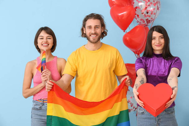 Man en twee mooie vrouwen met regenboog vlaggen en cadeau op kleur achtergrond. Begrip polyamorf en LGBT - Foto, afbeelding