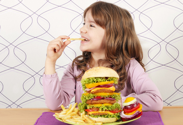 голодная маленькая девочка ест картошку фри и большой гамбургер
 - Фото, изображение