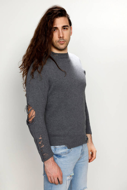Attractive young guy with very long curly hair is posing in studio. Style, trends, fashion concept. - Photo, Image