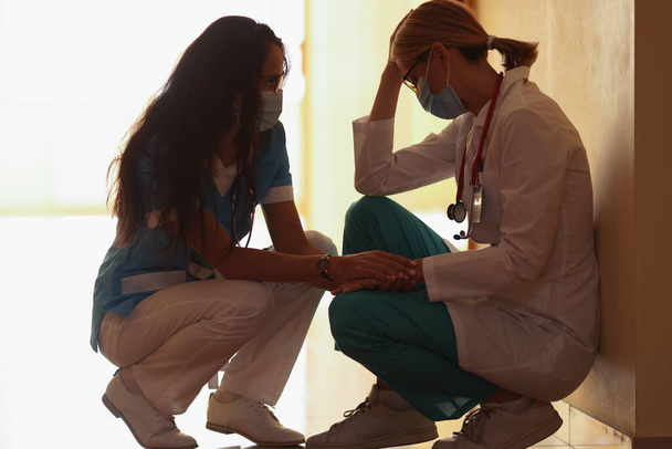 Een vrouwelijke arts kalmeert een vermoeide collega - Foto, afbeelding