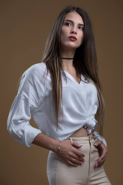 Portrait of a beautiful girl in a white shirt and leather leggings on a beige background - Foto, afbeelding