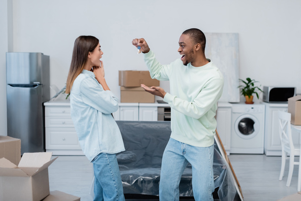 happy african american man holding key near excited girlfriend in new apartment - Foto, afbeelding