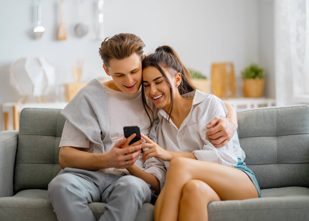 Young couple is using phone. Woman and man having fun staying at home. - Foto, imagen