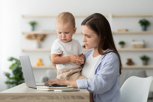 Mamá trabajadora. Mujer usando el ordenador portátil en casa y cuidando del bebé - Foto, imagen