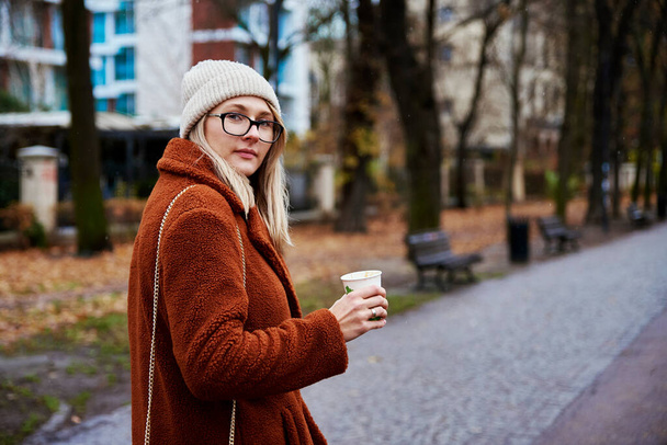 Young woman walking at city street with cup of coffee takeaway - Фото, зображення