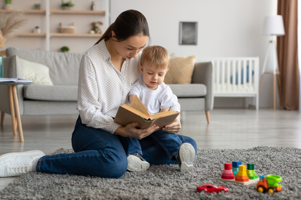 Babyentwicklung. Junge Mama liest Buch mit ihrem niedlichen Kleinkind Sohn zu Hause, Mutter verbringt Zeit mit ihrem Kind - Foto, Bild