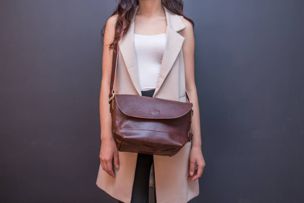 Woman holding brown leather bag on the gray background. Unisex bag - Photo, Image