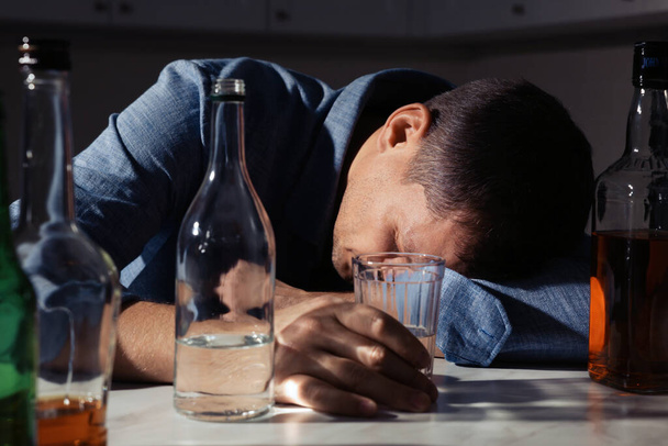 Addicted man with alcoholic drink sleeping at table in kitchen, closeup - Photo, Image