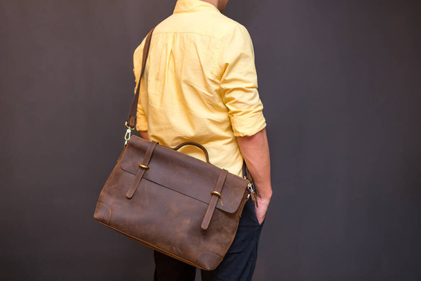 Man carries brown leather messenger bag in the hand on gray background. Unisex bag for sale. - Фото, изображение