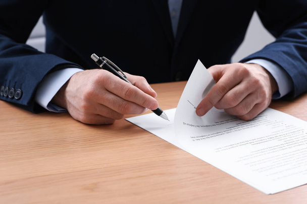 Businessman signing contract at wooden table, closeup of hands - Fotó, kép