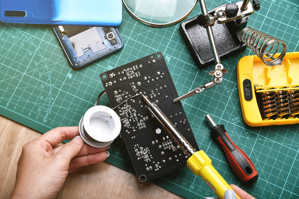 Elektronica reparatieservice, Technicus bevestigen van elektronische printplaat met soldeerbout en tin, Vergrootglas op soldeerstandaard. - Foto, afbeelding