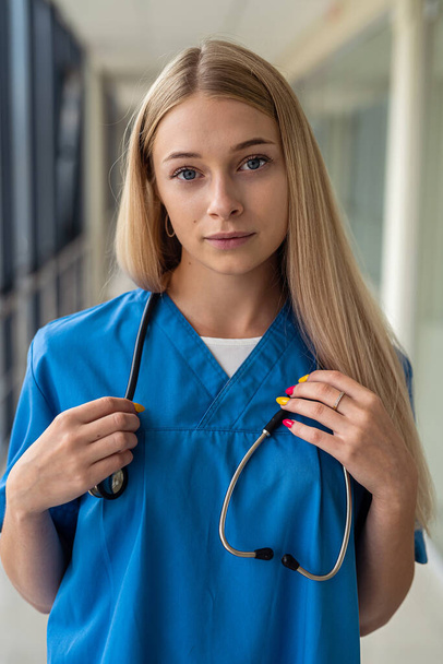 joven hermosa enfermera rubia encantadora con un estetoscopio se encuentra en el pasillo. Concepto de medicina - Foto, imagen