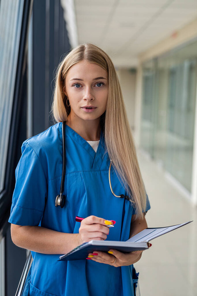bela enfermeira loira segurando um caderno com uma caneta no corredor do hospital. Conceito de medicina - Foto, Imagem