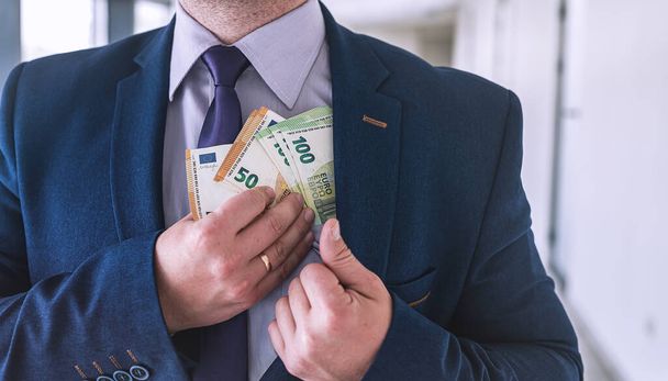 Επιχειρηματίας που βάζει χρήματα ευρώ στην τσέπη του, μισθό ή δωροδοκία έννοια της διαφθοράς - Φωτογραφία, εικόνα