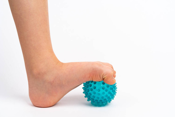 balle aiguille bleue pour massage et physiothérapie sur fond blanc avec un pied d'enfant, le concept de prévention et de traitement de valgus du pied - Photo, image