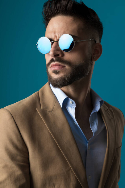 portret van aantrekkelijke jonge zakenman met retro bril op zoek naar kant op blauwe achtergrond - Foto, afbeelding