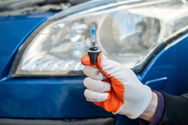 Mieshansikas käsi pitää gelagon-lamppua auton ajovalon taustalla. Auton korjaus käsite - Valokuva, kuva