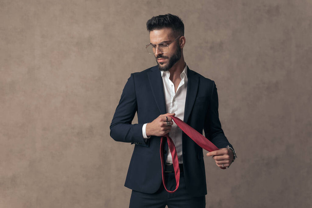 сексуальний драматичний бізнесмен, дивлячись вниз, тримає краватку і носить окуляри
 - Фото, зображення