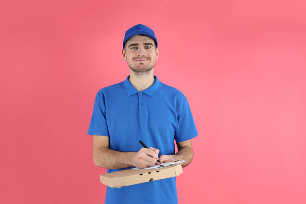Delivery man with pizza and clipboard on pink background - Photo, Image