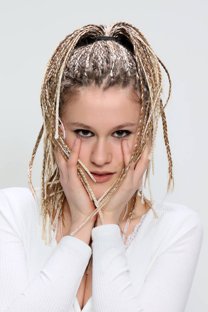 Adorable, teenage girl with blonde afro braids posing in studio on isolated background. Style, trends, fashion concept. - Фото, зображення
