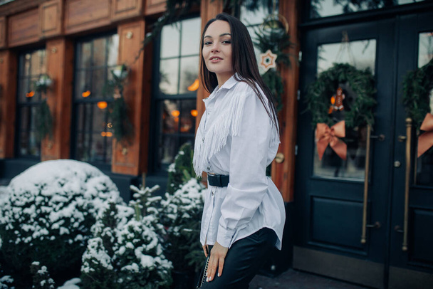 Young stylish brunette woman stands and smiles on street against background of building with Christmas decorations. Closeup. - Valokuva, kuva