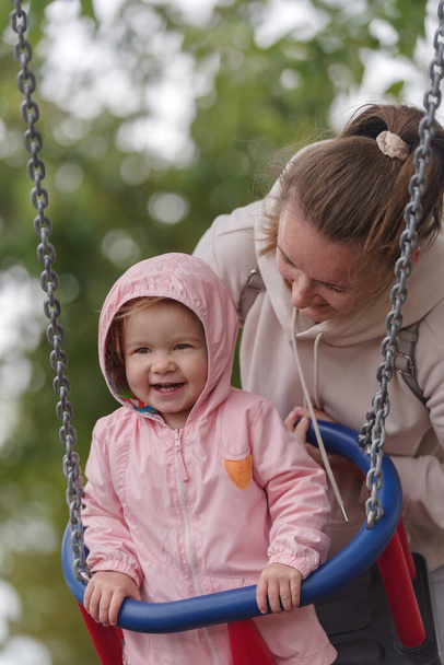 Meisje op swing met moeder in park - Foto, afbeelding