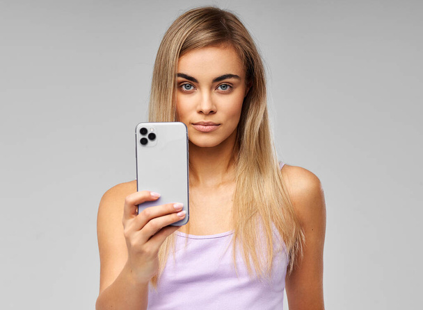 Young beautiful woman hold the mobile phone isolated on gray background - Fotó, kép