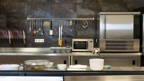 Cuisine ouverte d'un restaurant moderne avec réfrigérateur et fours, ustensiles de cuisine, couteaux, fouets, casseroles - Photo, image