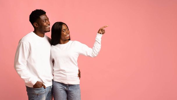 Liebendes afrikanisch-amerikanisches Paar umarmt und zeigt auf Kopierraum - Foto, Bild