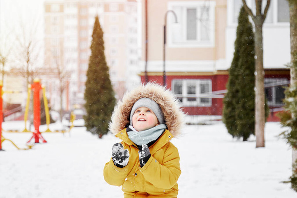 市内の雪の中で楽しい時間を過ごしている幸せな子供。外で冬の楽しみ。明るいオレンジの冬のジャケットの男の子。高品質の写真 - 写真・画像
