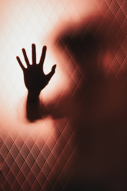 Detrás de la puerta de cristal moleteada la mano de una mujer inclinada pide ayuda - Foto, Imagen