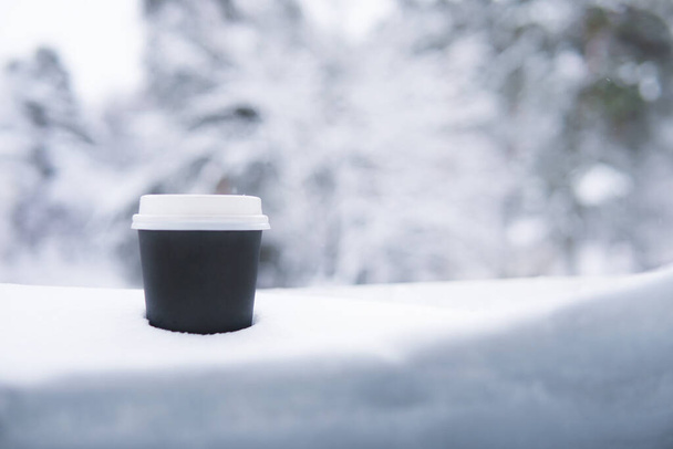 A black paper glass in the snow in winter. Coffee. Copy space - Фото, изображение