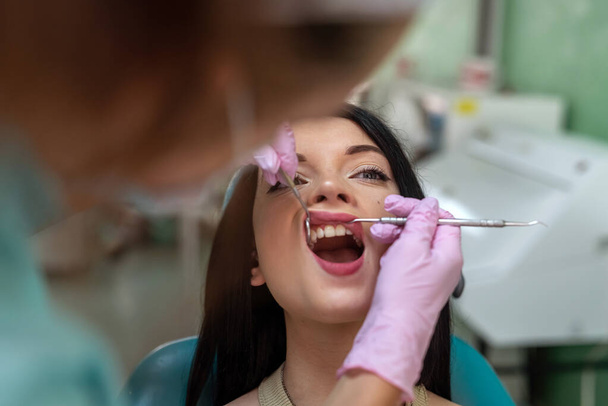 Kavkazský lékař vyšetří zuby pacienta zubním nástrojem, zdravotní a stomatologickou koncepcí - Fotografie, Obrázek