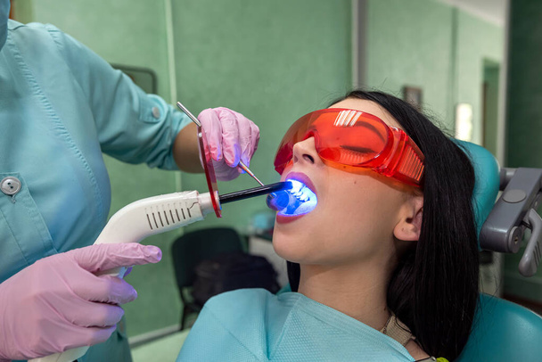 female dentist performing dental patient filling using UV lamp. Teeth whitening procedure - Photo, Image