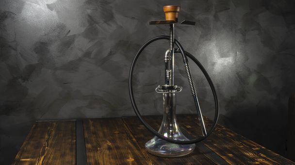 Modern hookah with glass bowl on wooden table. Gray wall background. - Fotó, kép