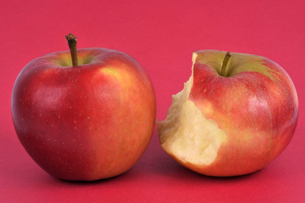 Целое яблоко и укусил яблоко крупным планом на красном фоне - Фото, изображение