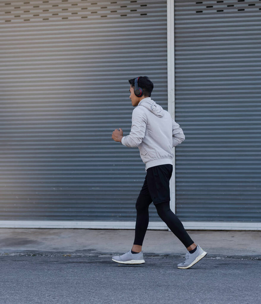 Młody mężczyzna ubrany w sportowy strój i słuchawki na głowie, biegający po drodze, ćwiczący, rozmazany blask dookoła - Zdjęcie, obraz
